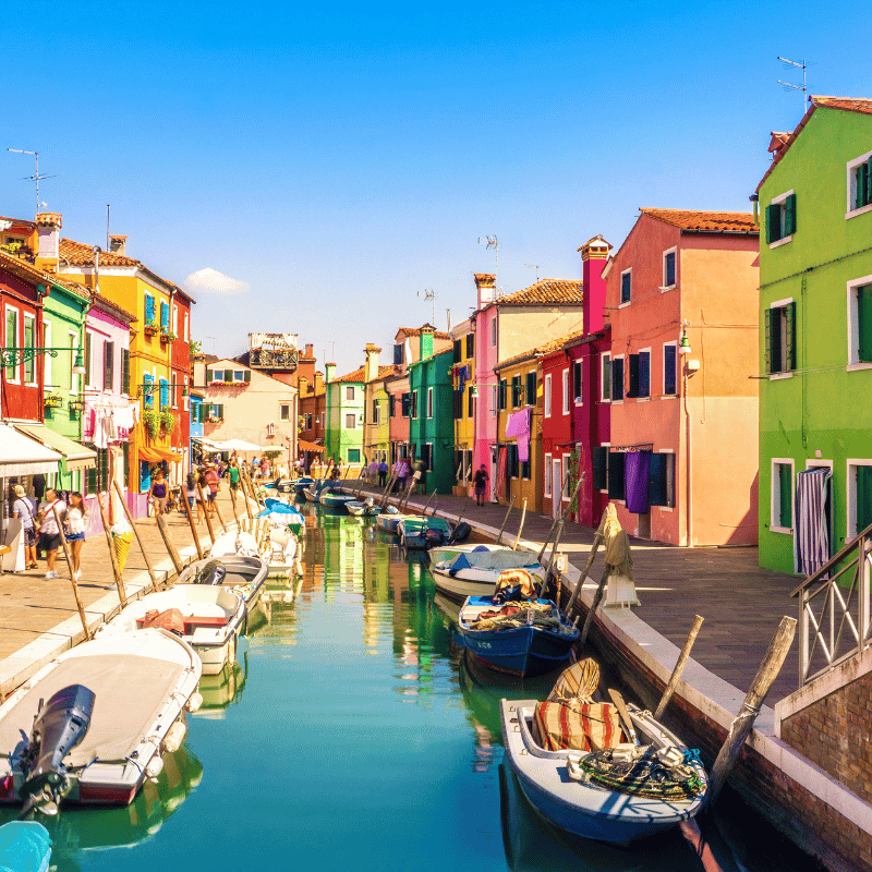 View of Venice, Italy, featuring the Grand Canal with historic palaces lining the water and gondolas moving through the canal under a bright sky.