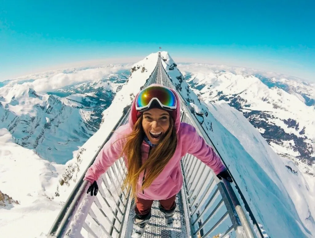 Traveller smiling on a suspension bridge between snowy Alpine peaks