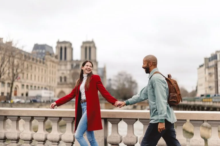 Couple walking hand in hand across a bridge in Paris, Notre-Dame behind them